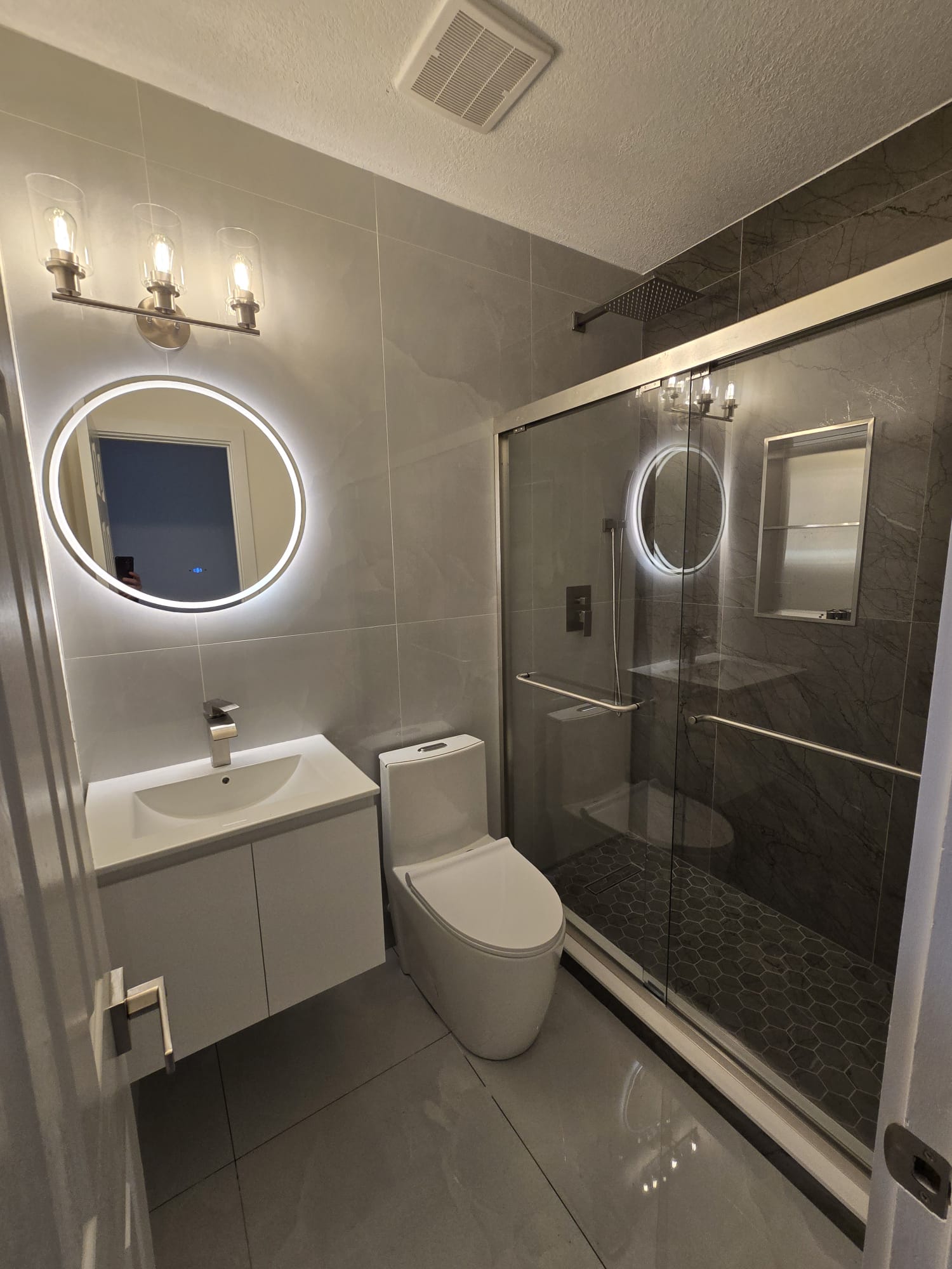 Baño con espejo circular iluminado y ducha de vidrio