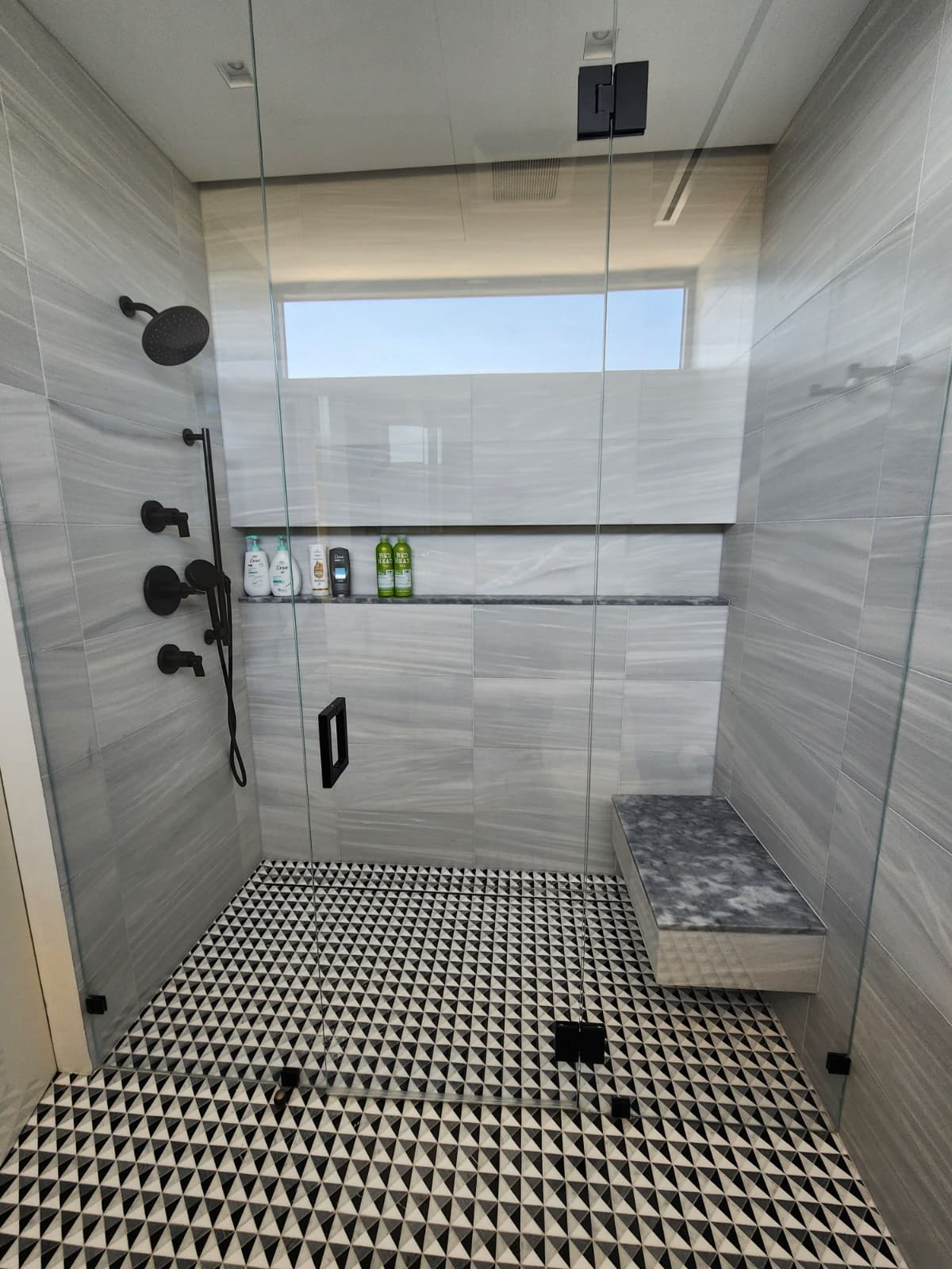 Ducha amplia en tile gris con banco y piso geométrico