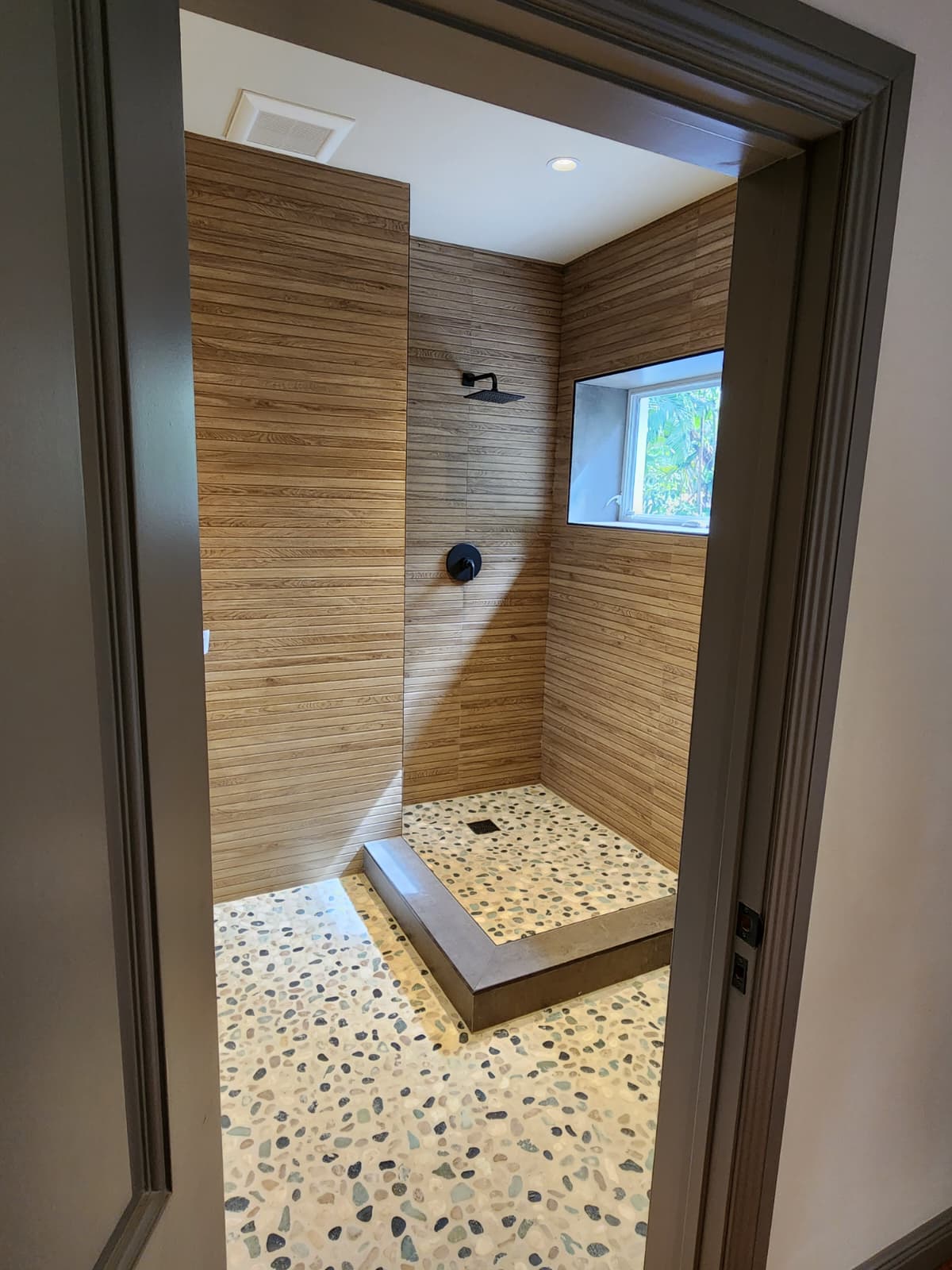 Ducha con revestimiento tipo madera y piso de piedra